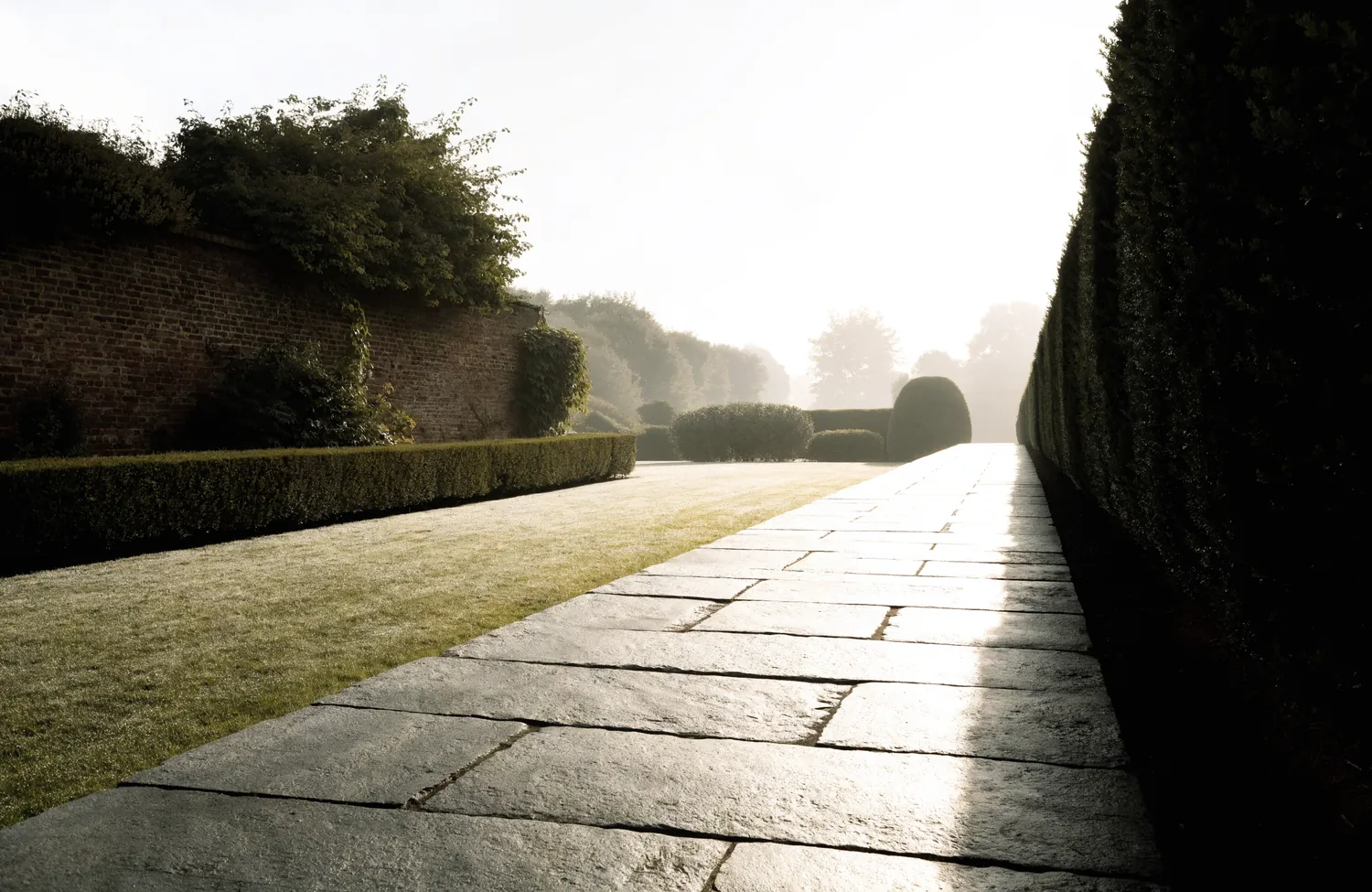 Gartenanlage mit geschnittenen Hecken und Natursteinweg im Morgennebel